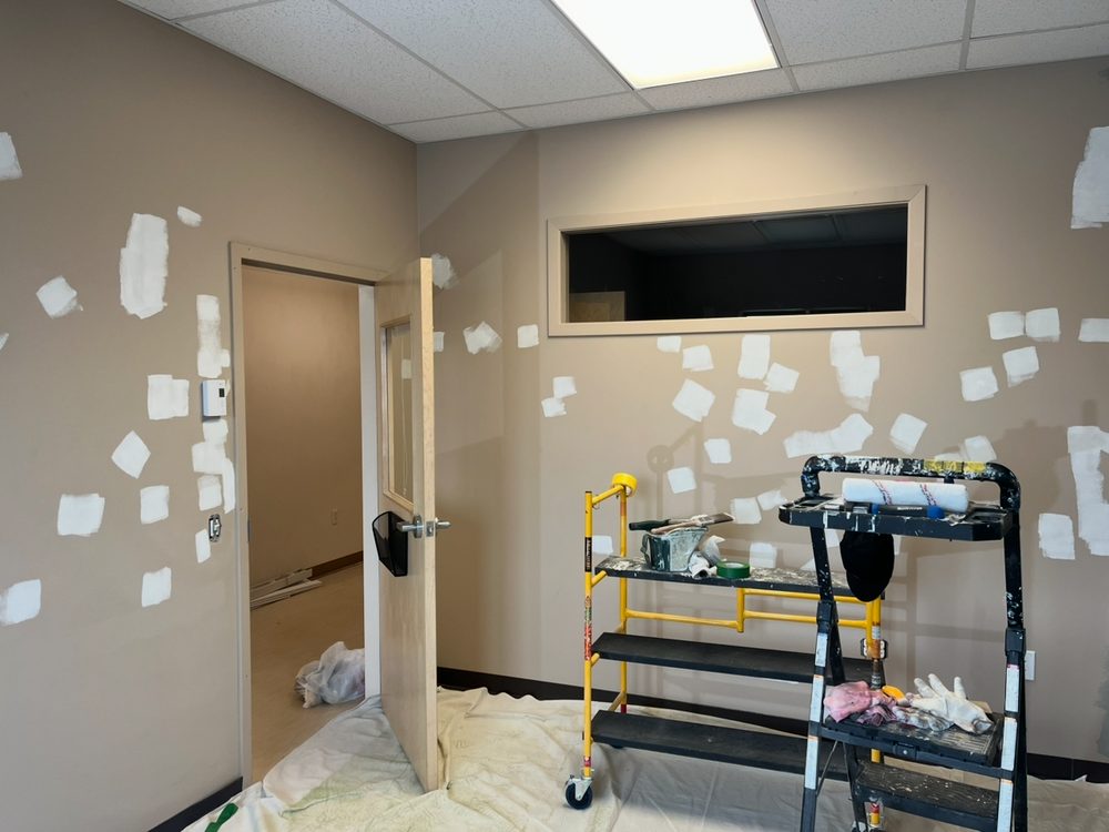 Office wall patched and sanded before repainting, interior window visible